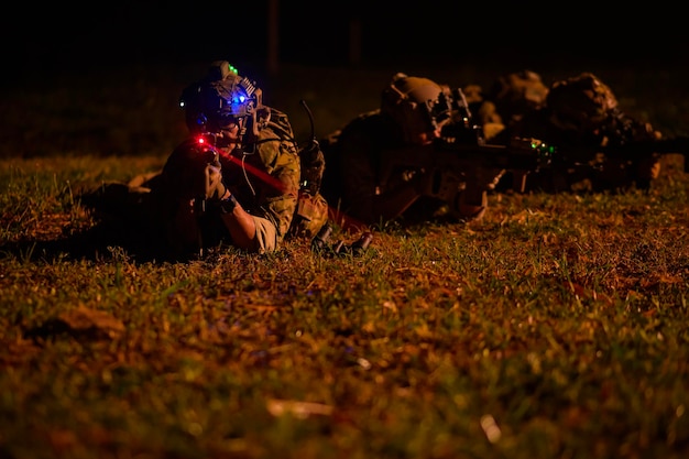 Des soldats en uniforme de camouflage visant avec leurs fusils pendant une opération militaire de nuit.