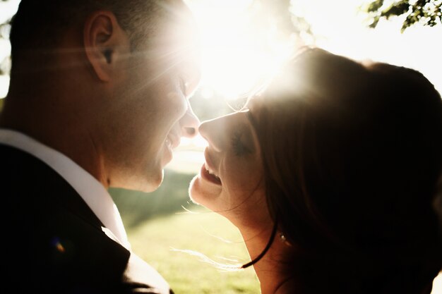 Le soleil brille sur la tête des jeunes mariés pendant qu&#39;ils se sourient avant un baiser