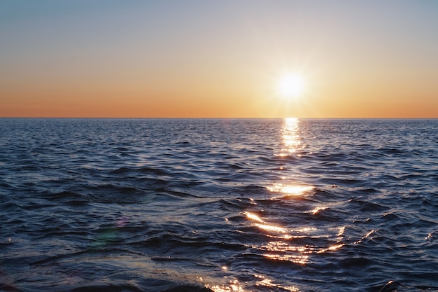 Photo le soleil couchant se jette dans la mer à l'horizon avec une piste lumineuse et des reflets sur la mer.