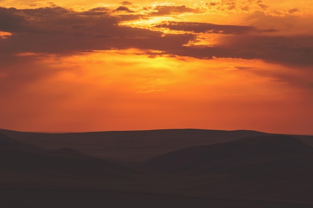 Soleil coucher de soleil lever du soleil Photo instantanée aux tons colorés Les rayons orange et jaune vif du soleil brillent derrière les nuages sur un ciel orange au-dessus des collines