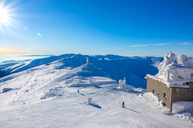 Soleil dans le ciel bleu sur les sommets des montagnes d'hiver. Bâtiment couvert de glace de la station supérieure des remontées mécaniques