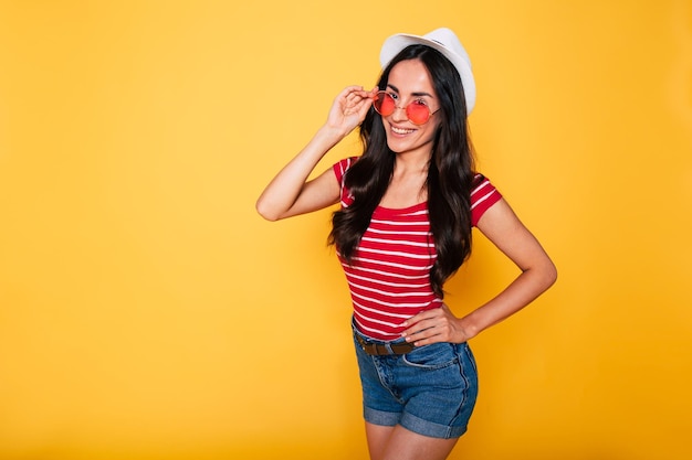 Soleil et détente sur la plage Heureuse belle jeune femme hipster en chapeau et lunettes de soleil posant sur fond jaune Heure d'été