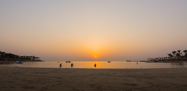 Soleil orange chaud au lever du soleil avec des plongeurs sur la plage dans le panorama égyptien