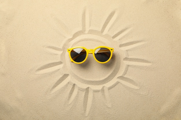 Photo soleil peint et lunettes jaunes sur sable de mer
