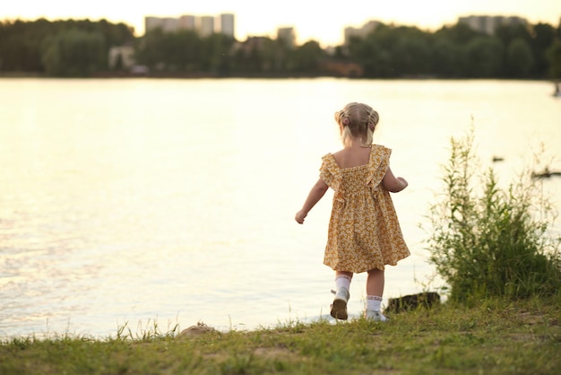 Le soleil plonge sous l'horizon, un enfant en bas âge se tient devant un lac serein, des marguerites à la main, une raison impérieuse