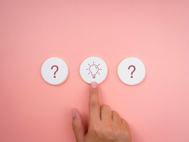 La solution, l'idée créative et l'innovation, la recherche d'une réponse aux concepts de réussite, un style minimal. Symbole d'icône d'ampoule et de point d'interrogation sur une éponge ronde blanche avec le choix de la main sur fond rose.