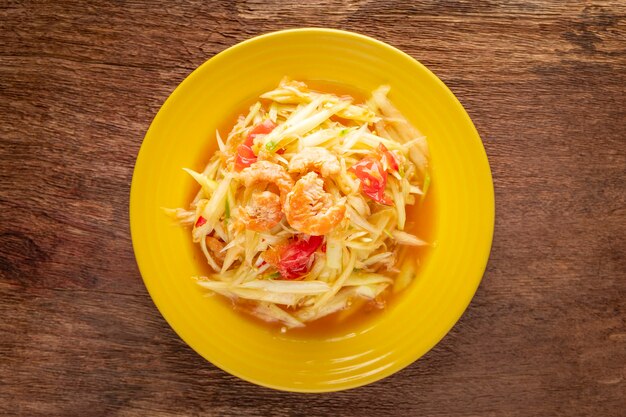 Som Tum Thai, Som Tam Thai, cuisine thaïlandaise, salade de papaye épicée avec garniture de tomate, citron vert et piment avec crevettes séchées sur fond de texture de bois naturel, vue de dessus