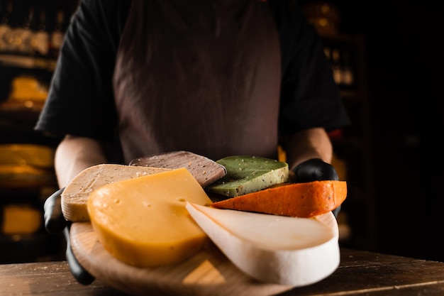 Sommelier au fromage tenant une assiette avec un mélange de jeunes fromages Gouda à la lavande de chèvre et de fromages au pesto vert et rouge sur la table Idée créative pour la publicité d'une fromagerie