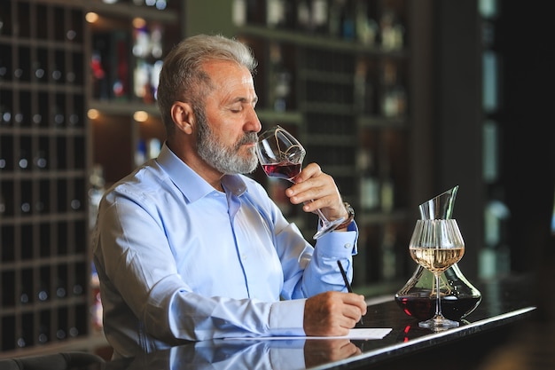 Un sommelier senior est en train de déguster du vin rouge.