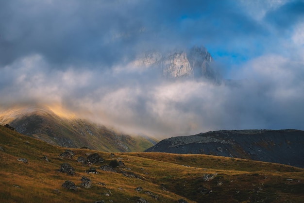 Un sommet de montagne dans les nuages avec un ciel nuageux en arrière-plan.