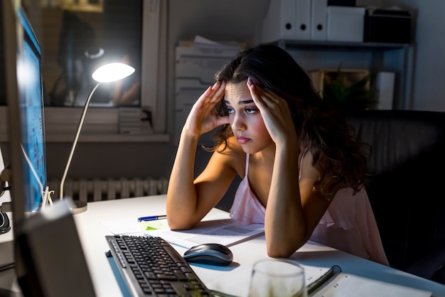 Somnolente femme épuisée travaillant au bureau avec son ordinateur, ses yeux se ferment et