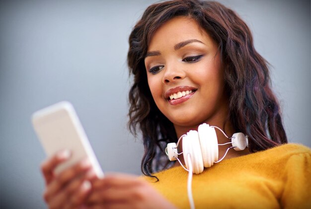 Son amie vient de lui envoyer une chanson à écouter Prise de vue en studio d'une jeune femme avec des écouteurs autour du cou à l'aide d'un téléphone portable sur fond gris