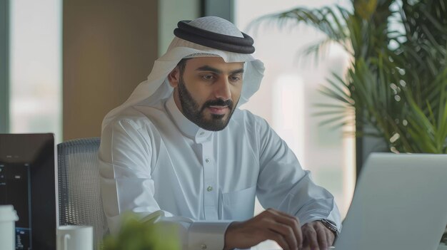 À son bureau dans son bureau, un beau jeune homme d'affaires arabe travaille avec un ordinateur portable.