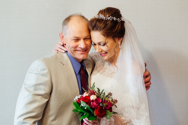 Son père embrasse sa fille à la mariée qui tient un bouquet de mariée dans ses mains