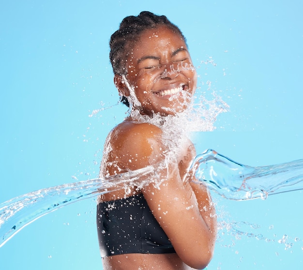 Son sourire est rayonnant. Photo d'une belle jeune femme éclaboussée d'eau sur un fond bleu.