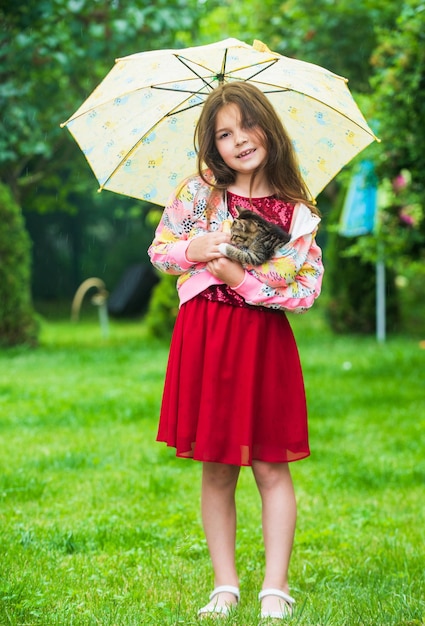 Son temps pluvieux petite fille tient un chaton enfant aime son animal de compagnie humain et les animaux aiment et soignent un chat moelleux dans la main d'un joli enfant petite beauté en plein air sous un parapluie enfance heureuse amoureux des animaux