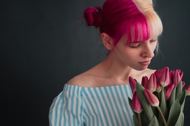 songeuse jeune femme aux cheveux roses tenant un bouquet de tulipes sur fond noir