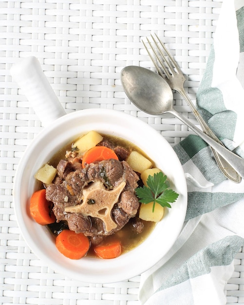 Sop Buntut ou soupe de queue de boeuf servie dans un bol blanc sur une vue de dessus de table tissée blanche