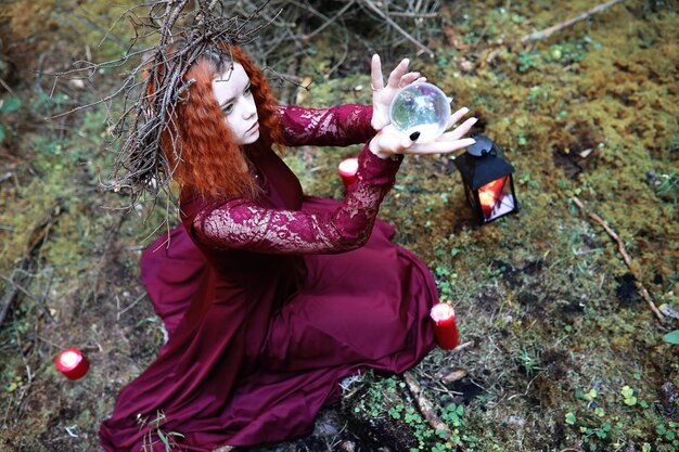 Photo la sorcière aux cheveux roux organise un rituel avec une boule de cristal dans la forêt