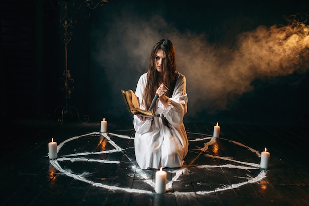 Sorcière en chemise blanche tient un couteau et lit le sort