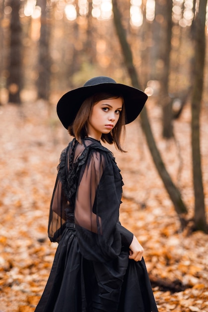 Sorcière dans la forêt d'automne. Une fille vêtue d'une longue robe noire se promène dans la forêt.