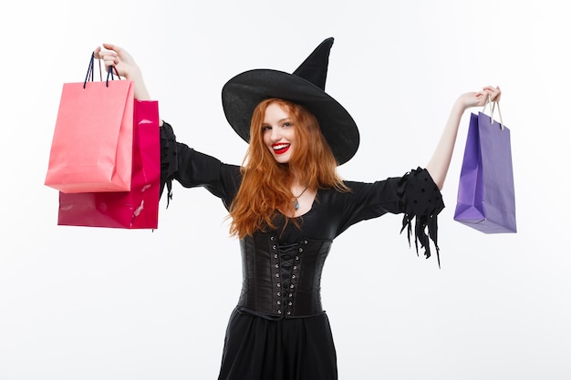 Sorcière d&#39;Halloween heureux souriant et tenant des sacs à provisions colorés sur fond blanc.