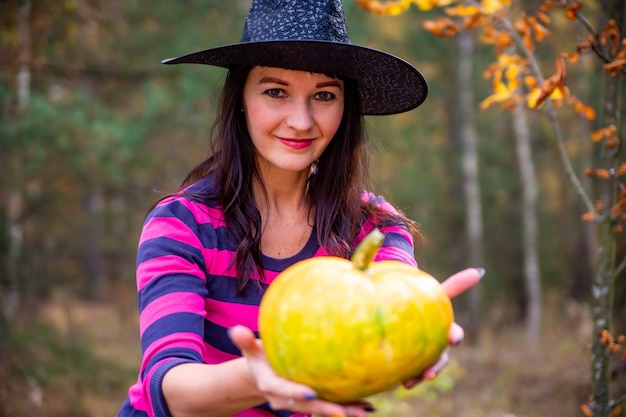 La sorcière tend une citrouille à la caméra dans la forêt d'automne