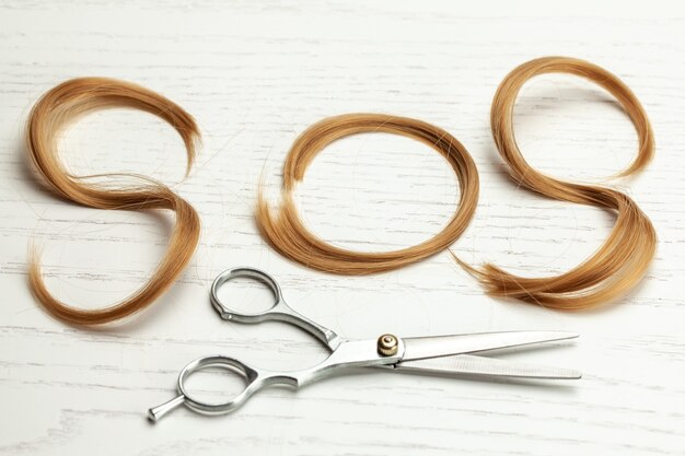 SOS d'une mèche de cheveux. Problème de cheveux et coupe de cheveux aux ciseaux. Surface en bois blanc.