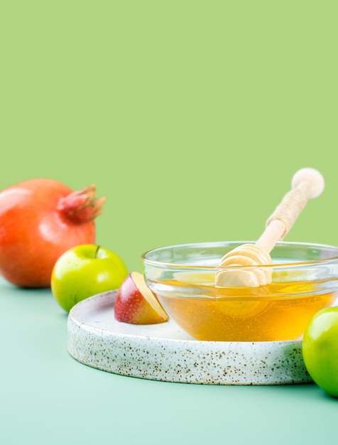 Soucoupe en verre avec du miel frais cuillère à miel pomme et grenade sur un fond vert clair Concept créatif Nouvel an juif Bonnes vacances Rosh Hashanah mise en page des symboles traditionnels