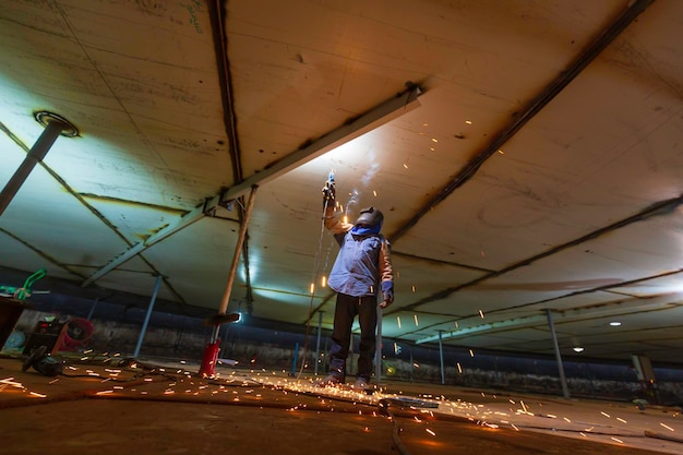 Le soudage du métal des travailleurs masculins fait partie de la construction de poutres de réservoir de toit de plaque de machines étincelle flash à l'intérieur d'espaces confinés