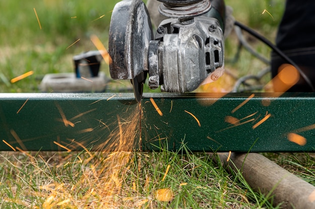 soudeur à l'aide d'une meuleuse de métal pour couper un métal sur l'herbe dans le village , des éclairs lumineux