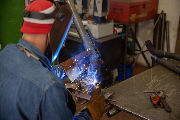 Soudeur dans l'usine soudant une pièce métallique portant un écran facial et des gants de protection