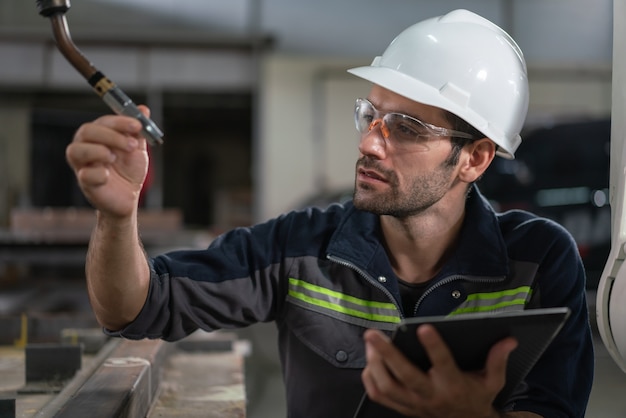 Soudeur ingénieur en automatisation mâle vérifiant la tête de soudage du robot avec spécification de données sur tablette dans une usine industrielle