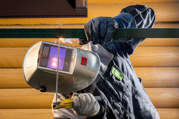 Le soudeur masculin de travailleur à un chantier de construction soude une structure métallique sur une barrière, processus de soudure