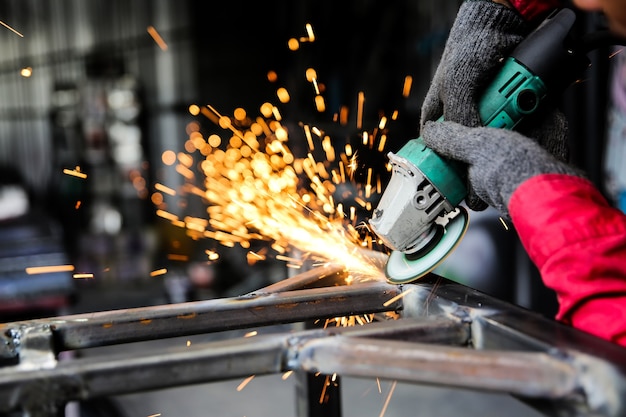 Le soudeur a utilisé la meule sur l'acier en usine avec des étincelles, le processus de soudage à l'atelier industriel, les mains avec l'instrument dans le cadre.