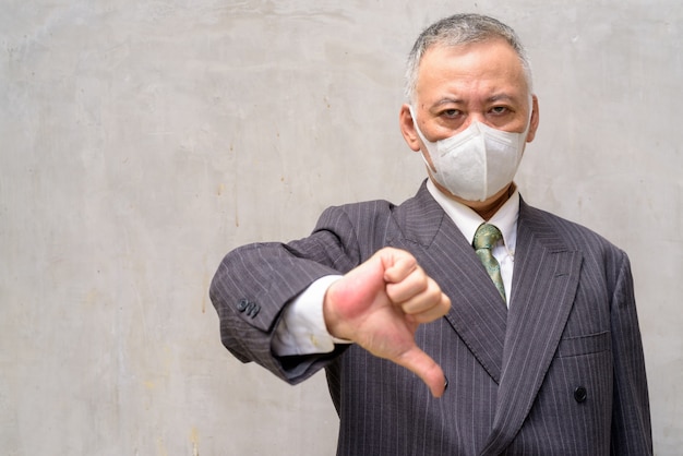 A souligné l'homme d'affaires japonais mature avec masque donnant les pouces vers le bas à l'extérieur