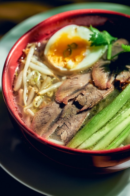 Soupe asiatique épicée du Sichuan avec nouilles, bœuf, œuf et concombre dans un bol.