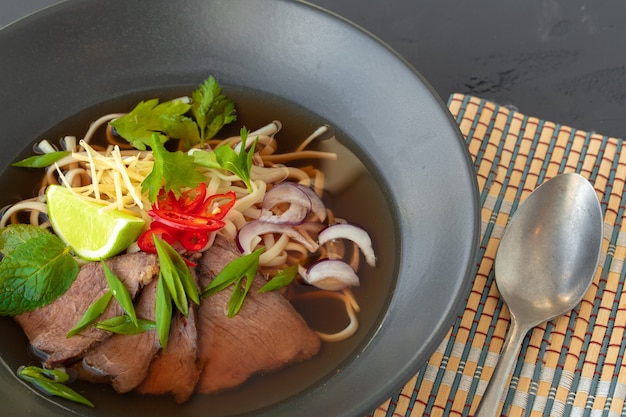 Soupe asiatique ramen servi dans un bol noir sur table grise