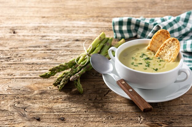 Soupe d'asperges vertes fraîches dans un bol sur table en bois.