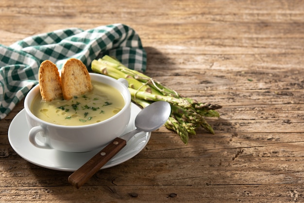 Soupe d'asperges vertes fraîches dans un bol sur table en bois