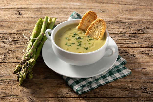 Soupe d'asperges vertes fraîches dans un bol sur table en bois