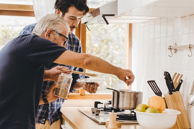 Soupe d'assaisonnement aux personnes âgées avec des ingrédients naturels cuisinant avec un jeune homme pour rester à la maison en famille.