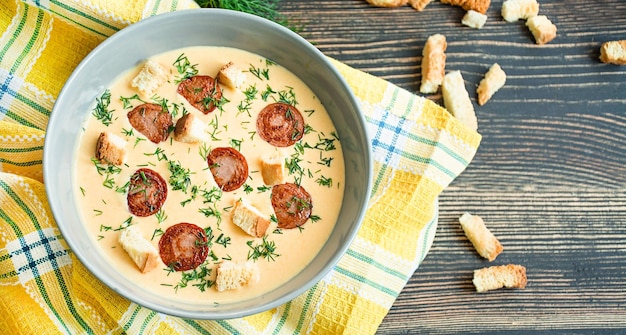 Soupe au fromage avec des saucisses grillées et des herbes Soupe à la crème servie dans une assiette Fond en bois foncé Espace pour le texte