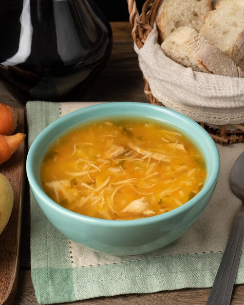 Soupe au poulet dans un bol avec des tranches de pain et du vin sur une table en bois