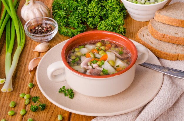 Soupe au poulet avec pois verts et légumes dans un bol sur un fond en bois