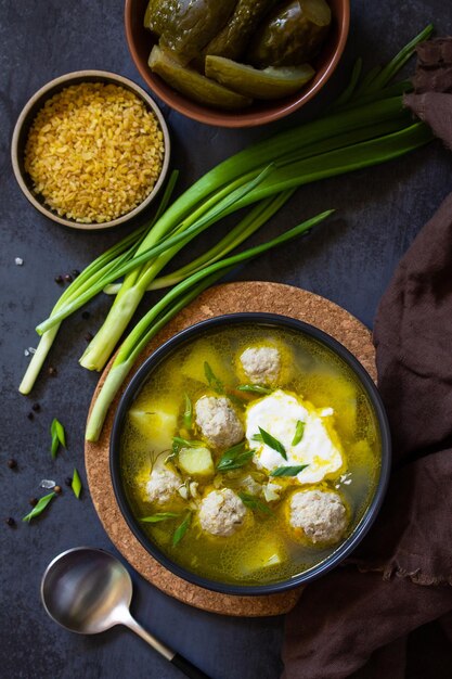 Soupe aux boulettes de boulgour et concombres marinés sur une table en pierre sombre Vue de dessus à plat