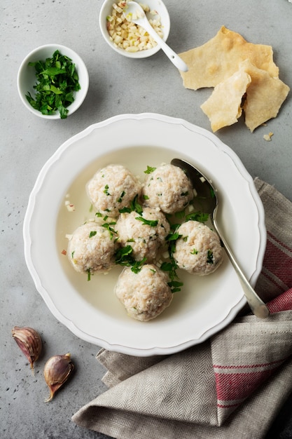 Soupe aux boulettes de poulet matzo maison avec du persil et de l'ail dans une simple plaque en céramique blanche sur une pierre grise ou du béton