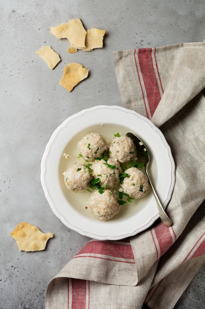 Soupe aux boulettes de poulet matzo maison avec du persil et de l'ail dans une simple plaque en céramique blanche sur une pierre grise ou du béton