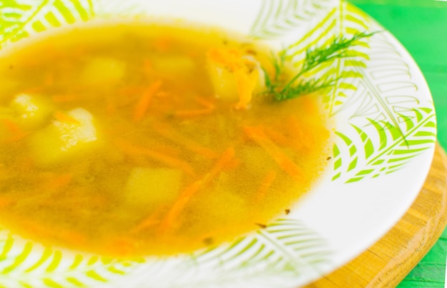 Soupe aux carottes viande pommes de terre et condiments dans une assiette dans une assiette sur un fond de bois vert