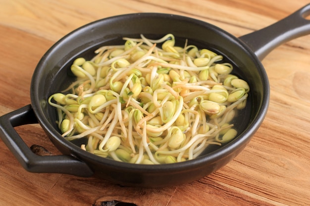 Soupe aux germes de soja (Kongnamul Guk) Rafraîchissante de style coréen, servie sur un bol noir, table en bois avec des oignons verts tranchés sur le dessus.